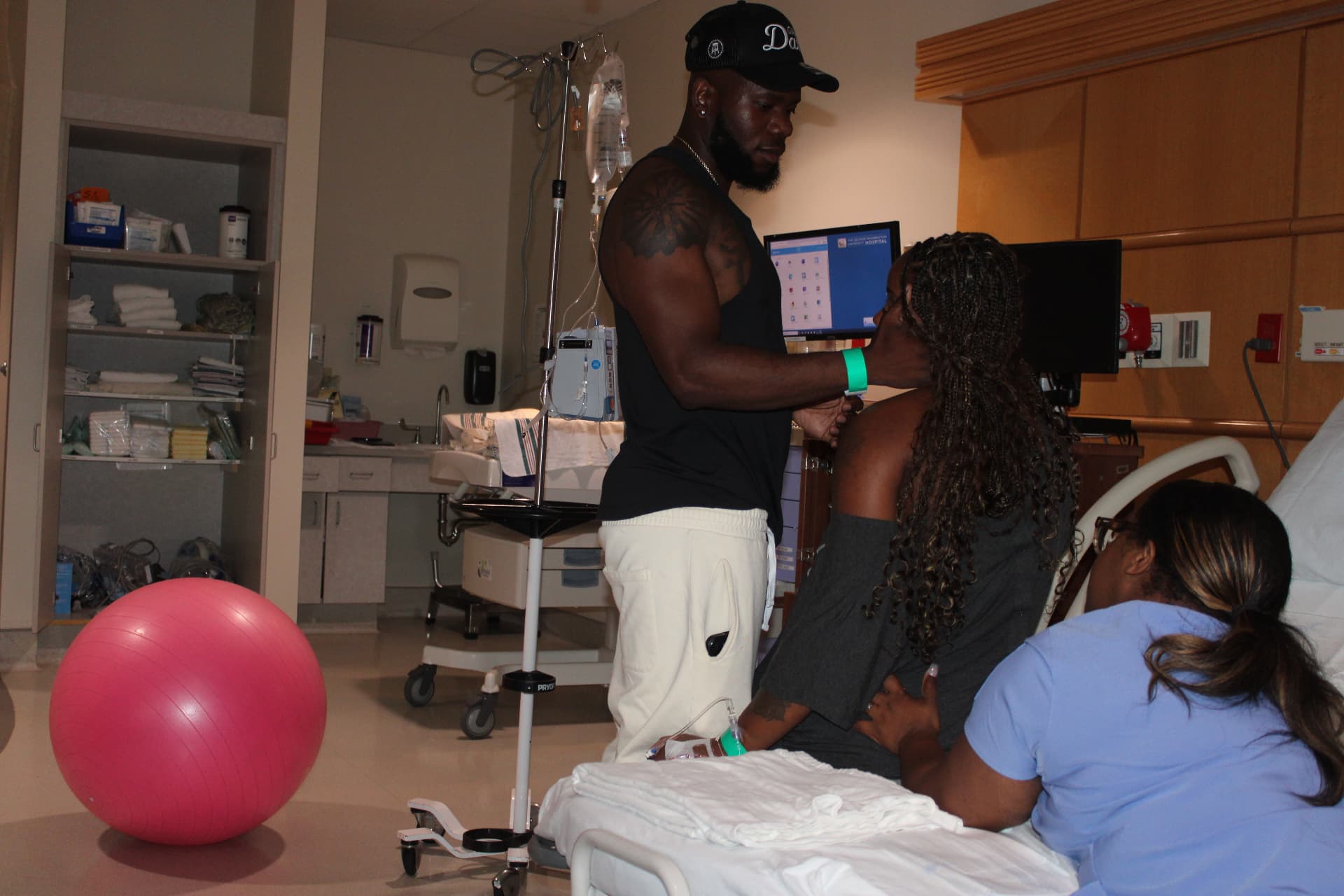 Partner standing to hold a laboring mother's hands while the doula supports her from the side of the bed