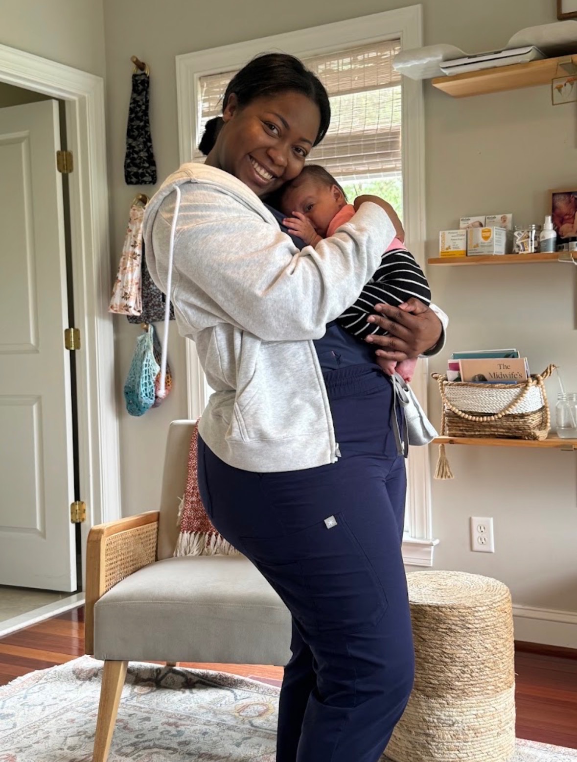 A doula in scrubs smiling while snuggling a newborn during a home visit