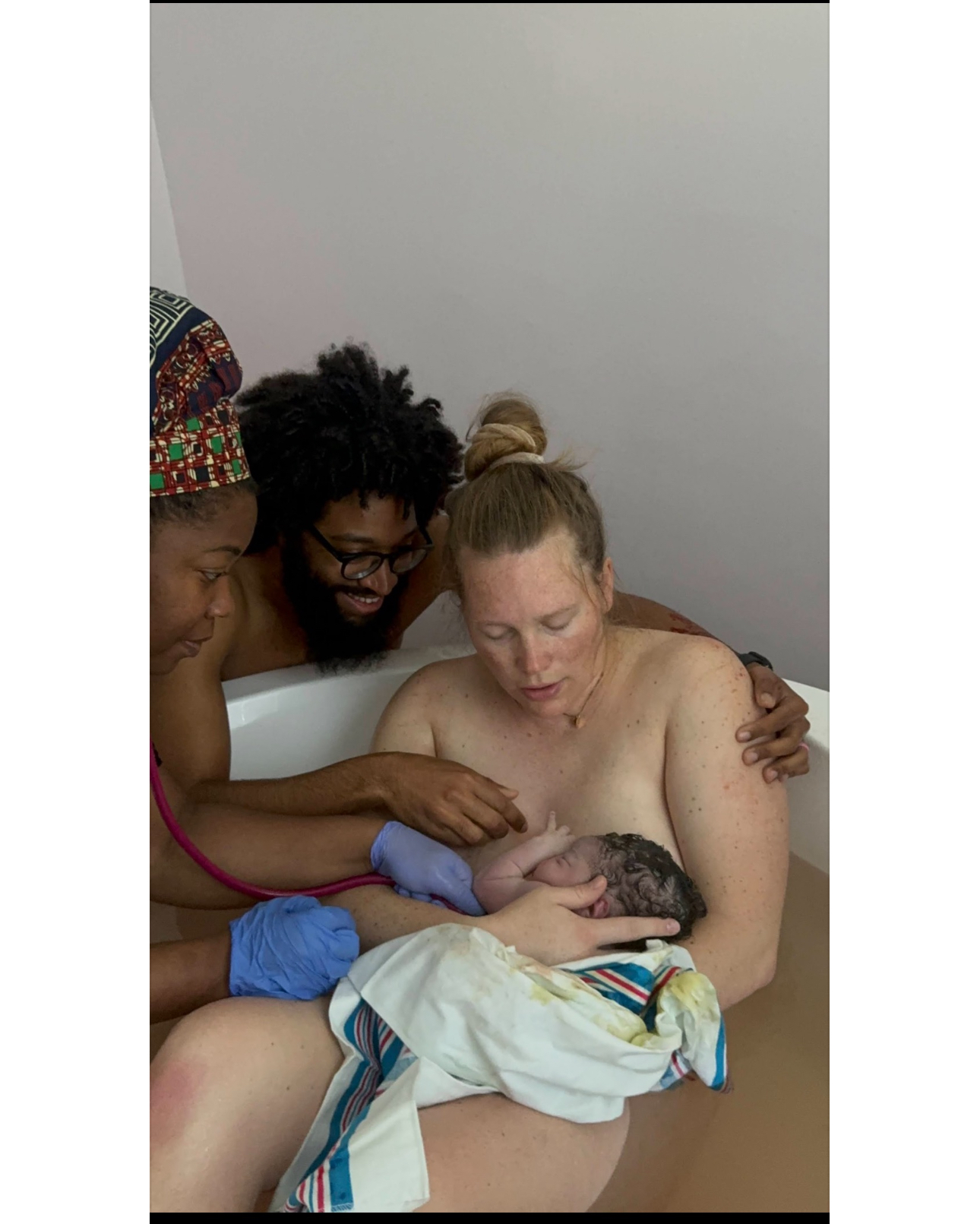 A mother holding her freshly born baby skin to skin in the birth tub while her partner and birth worker look on